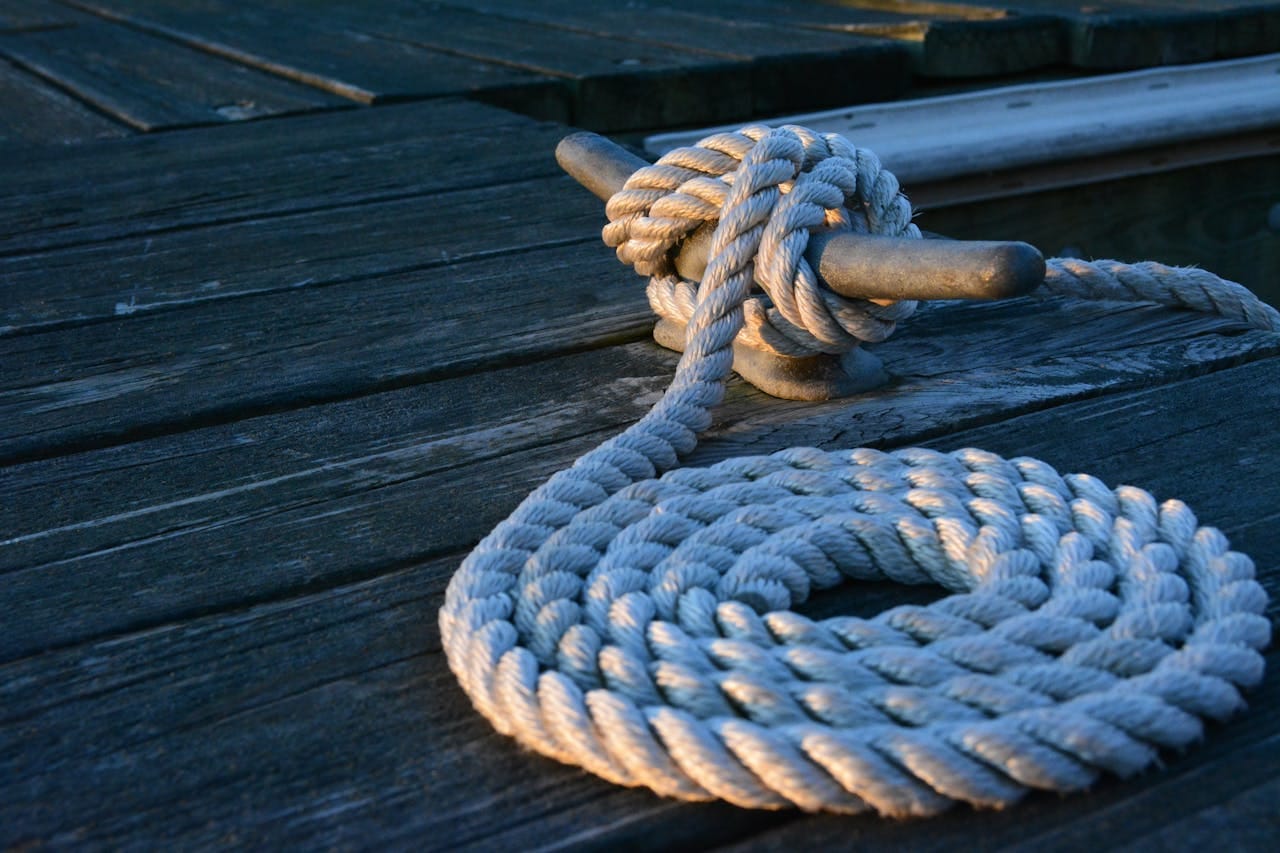 Close-up of a sturdy nautical knot on a weathered wooden dock at sunset.